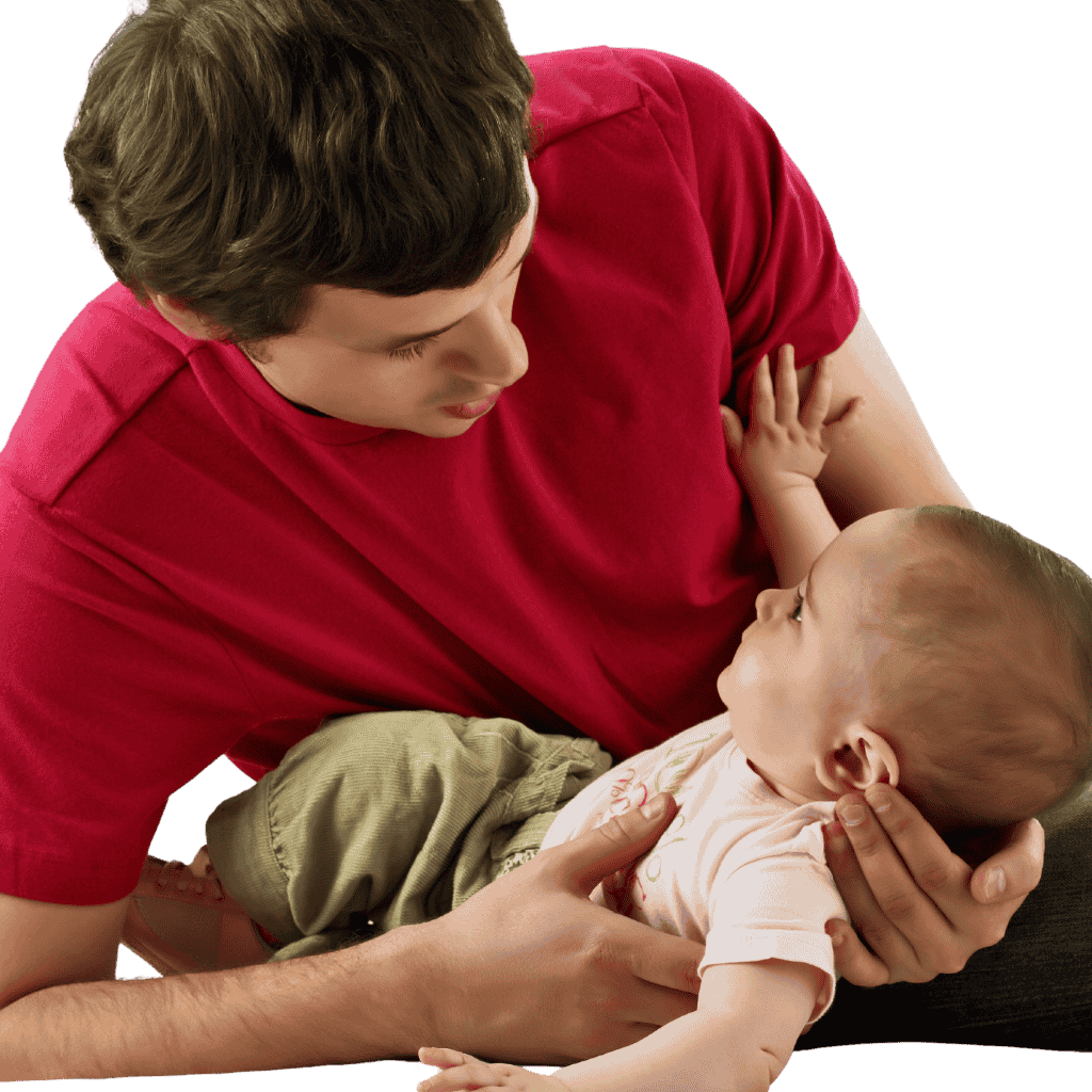 Man in a red shirt cradles a baby in his arms, looking down at the child with care.