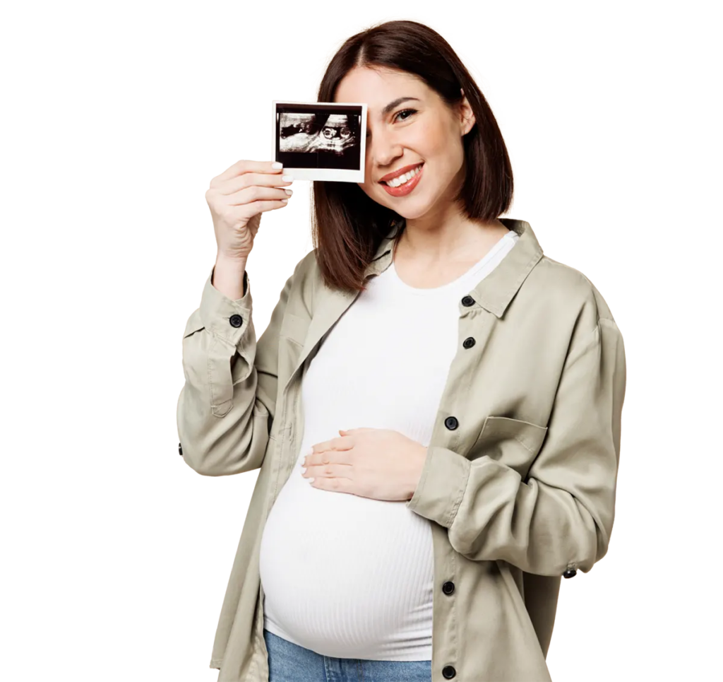 Pregnant woman holding an ultrasound photo up to the camera and smiling.